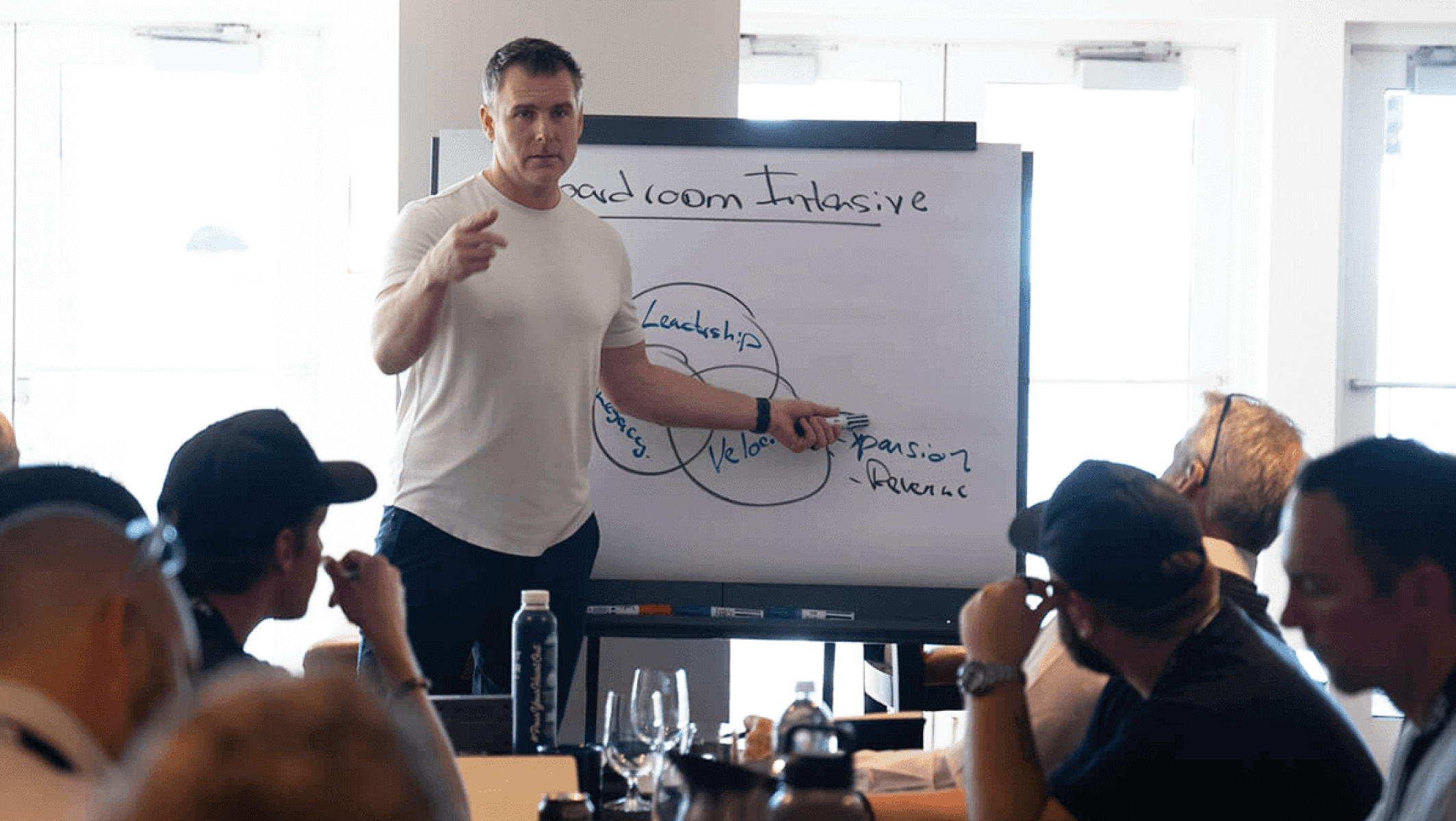 A man points to a whiteboard while addressing an audience